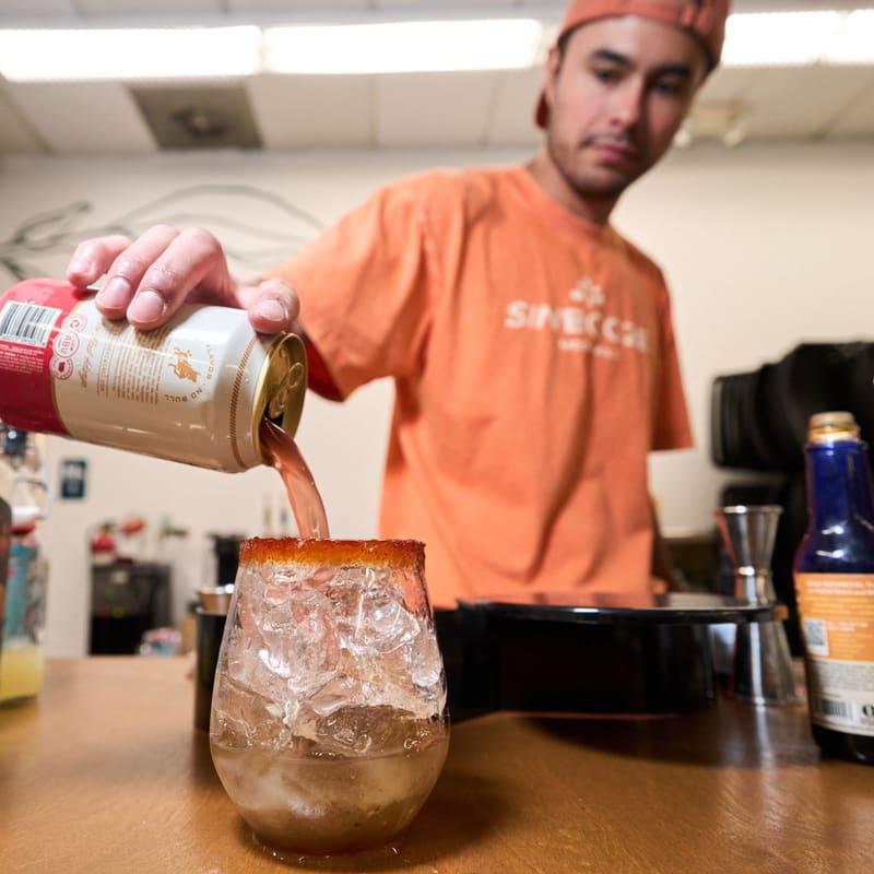 Aldo pours a drink over ice into a rimmed glass