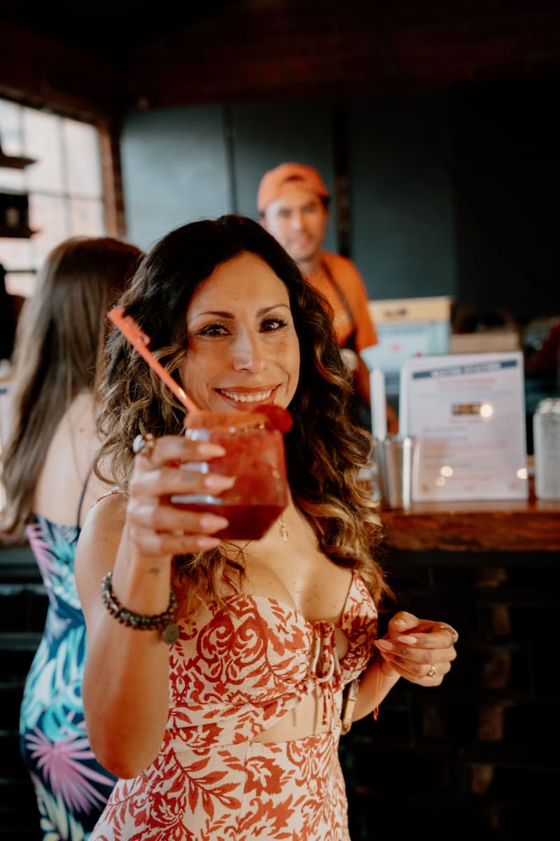 A guest smiles and holds up a red mocktail with a straw