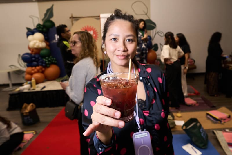 A guest holds a dark red mocktail toward the camera