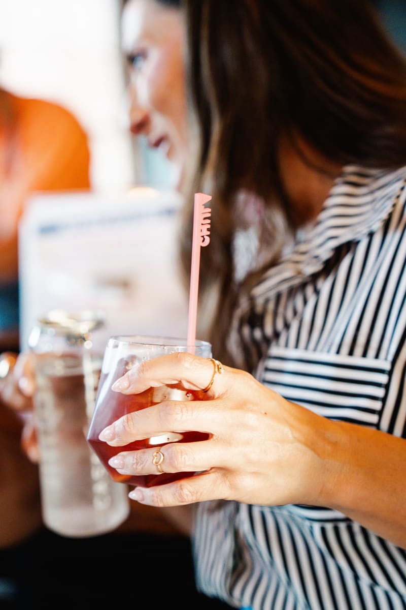 A guest's hand holds a mocktail with a pink stir stick