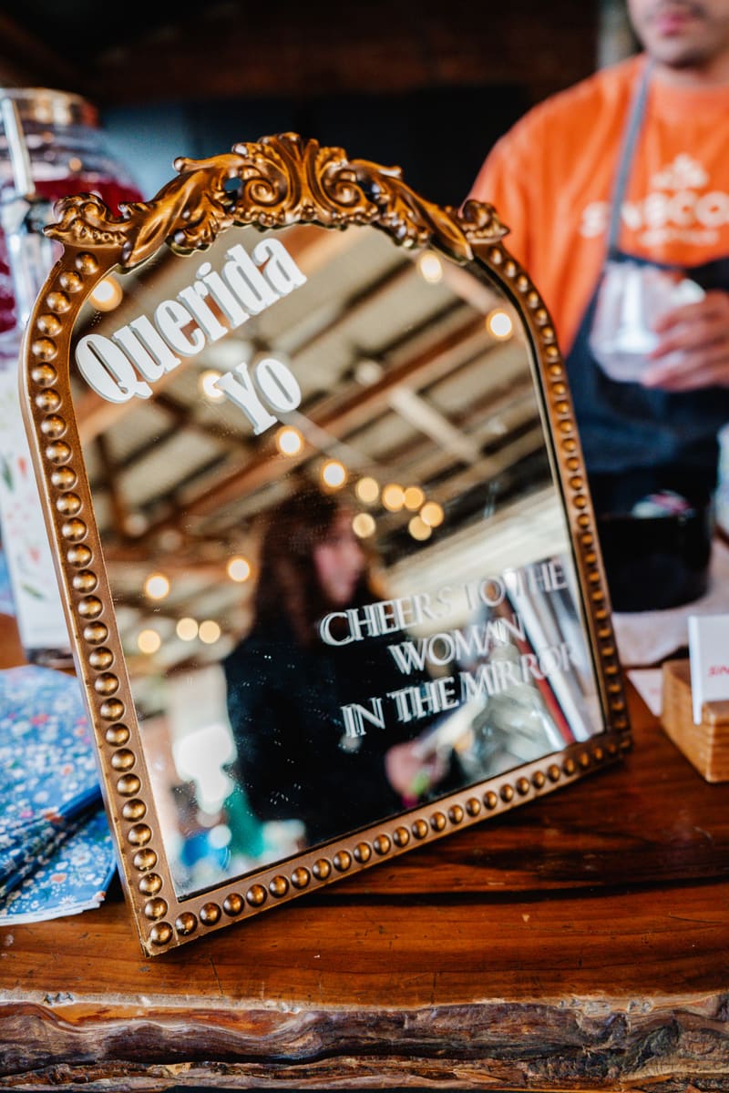 A Querida Yo mirror at an event, with Aldo serving drinks in the background
