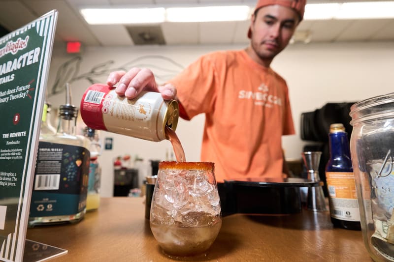Aldo pours a drink over ice into a rimmed glass behind the Sin Booze bar