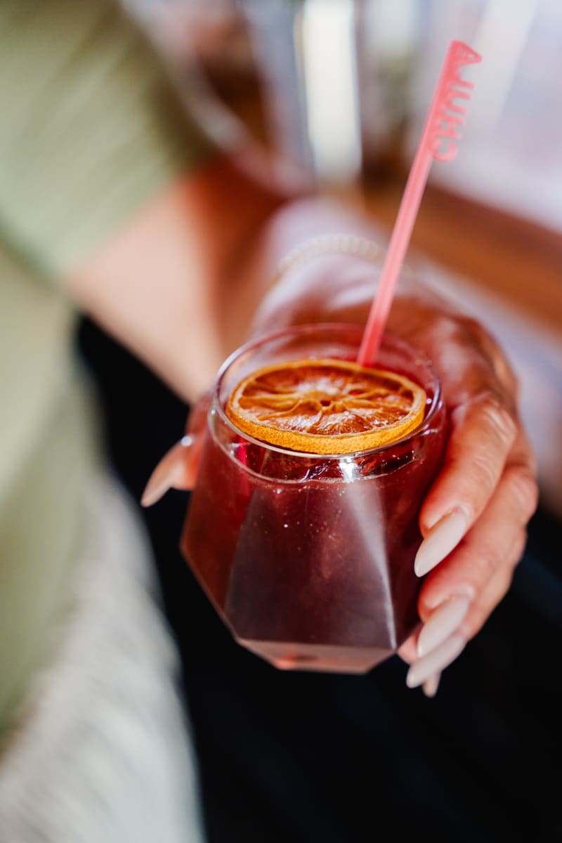 A guest holds a ruby-red Sin Booze mocktail garnished with a dried orange wheel